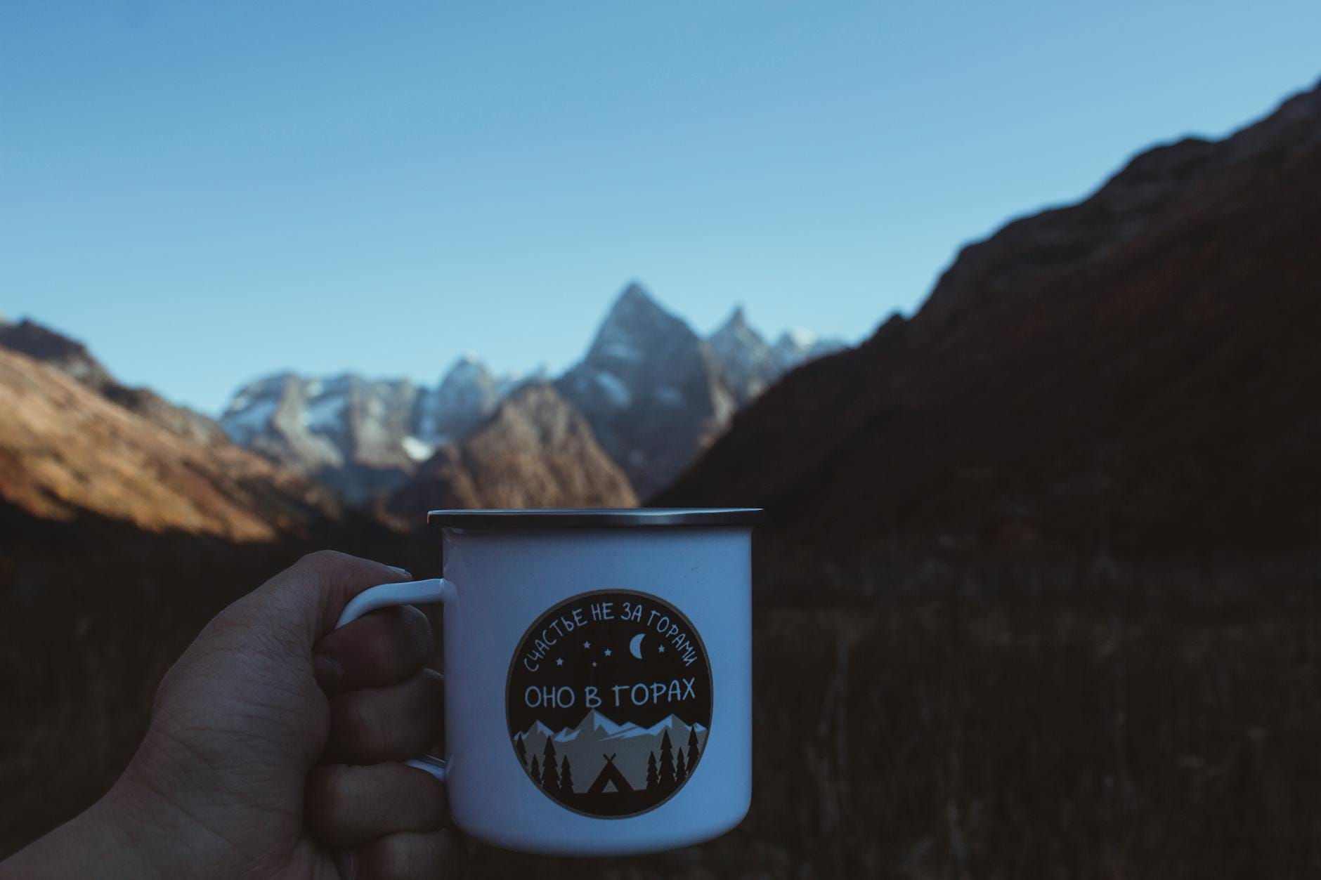 Dłoń z emaliowanym kubkiem na tle gór o wschodzie słońca