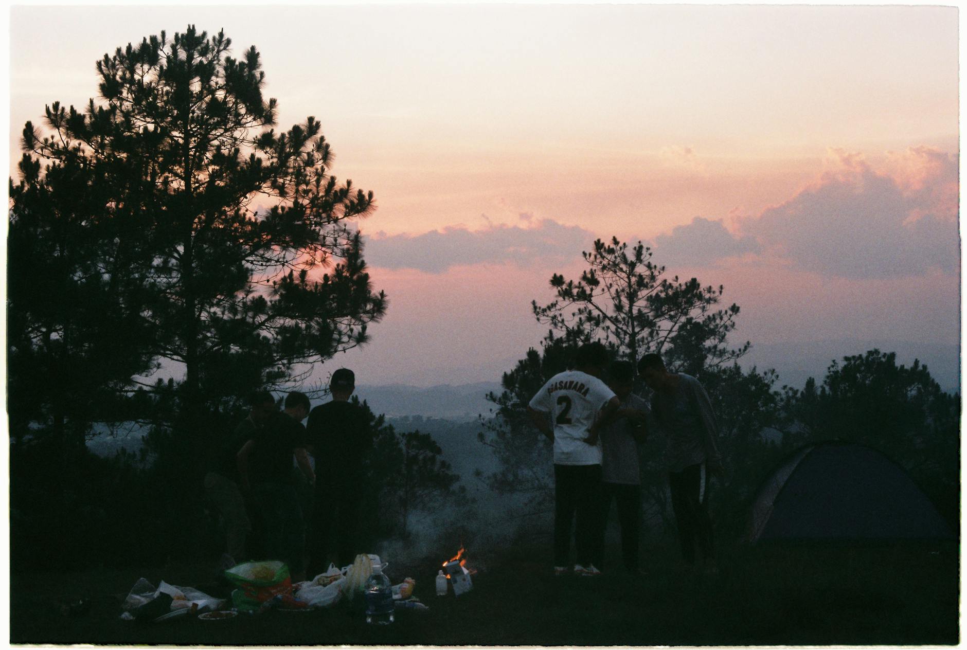 Grupa znajomych przy ognisku w lesie o zachodzie słońca