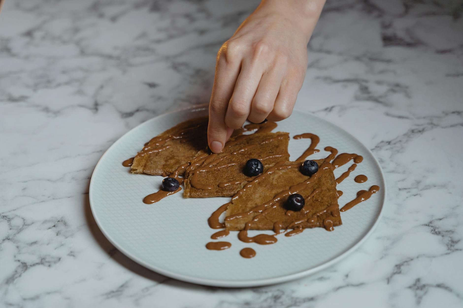Dłoń dekoruje naleśniki jagodami na jasnym marmurowym blacie