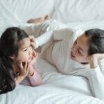 Mama i kilkuletnia córka leżą na łóżku i czule rozmawiają